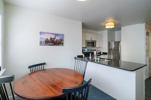 Una cocina moderna con armarios blancos, un refrigerador de acero inoxidable y una mesa de comedor de madera con sillas.
