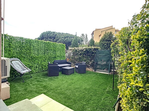 A backyard with a green lawn, outdoor furniture, and a tall hedge.