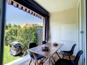 Ein Balkon mit Tisch, Stühlen, einem Grill und Blick auf einen Garten sowie Gebäude.