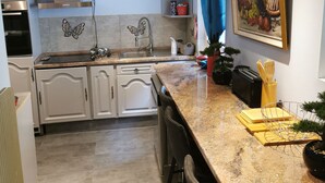 Eine moderne Küche mit weißen Schränken, Granit-Arbeitsplatten und einem Gemälde von Obst und Gemüse an der Wand.