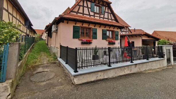 Ein traditionelles Fachwerkhäuschen mit geneigtem Dach, einem schwarzen Metallzaun und Blumenkästen an den Fensterbänken.
