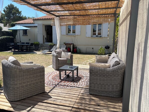 Ein Außenbereich mit Terrassenmöbeln aus Rattan, einem gemusterten Teppich und einer Pergola, die Schatten spendet.