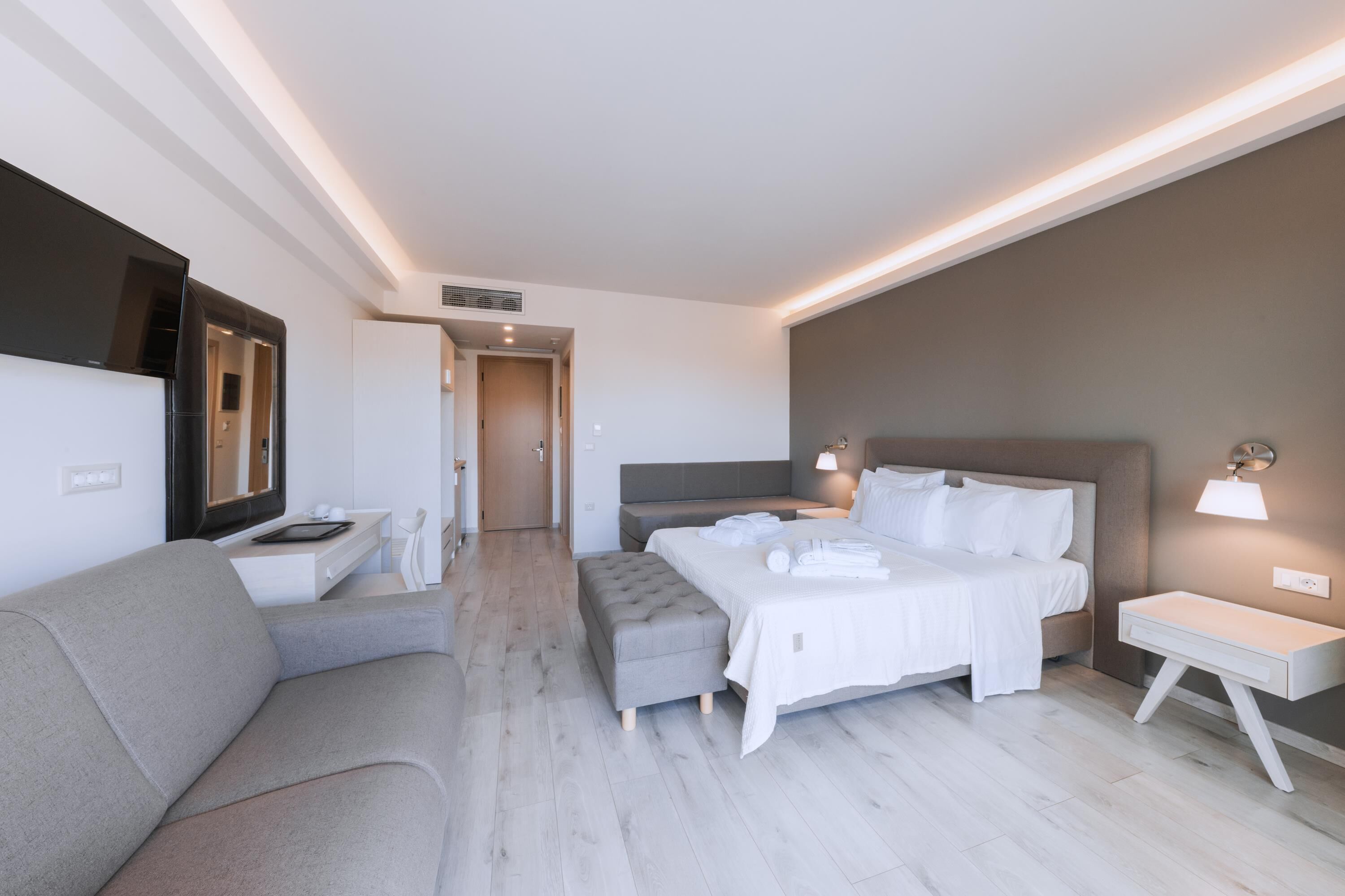 Una habitación de hotel moderna con cama, sofá, televisor y mesita de noche.