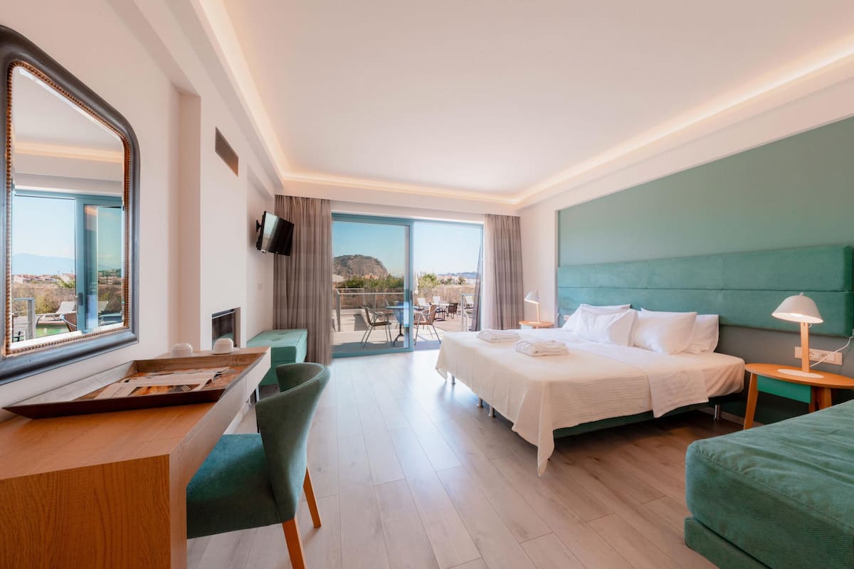 Habitación de hotel con cama, escritorio, silla, televisor y vistas al exterior.
