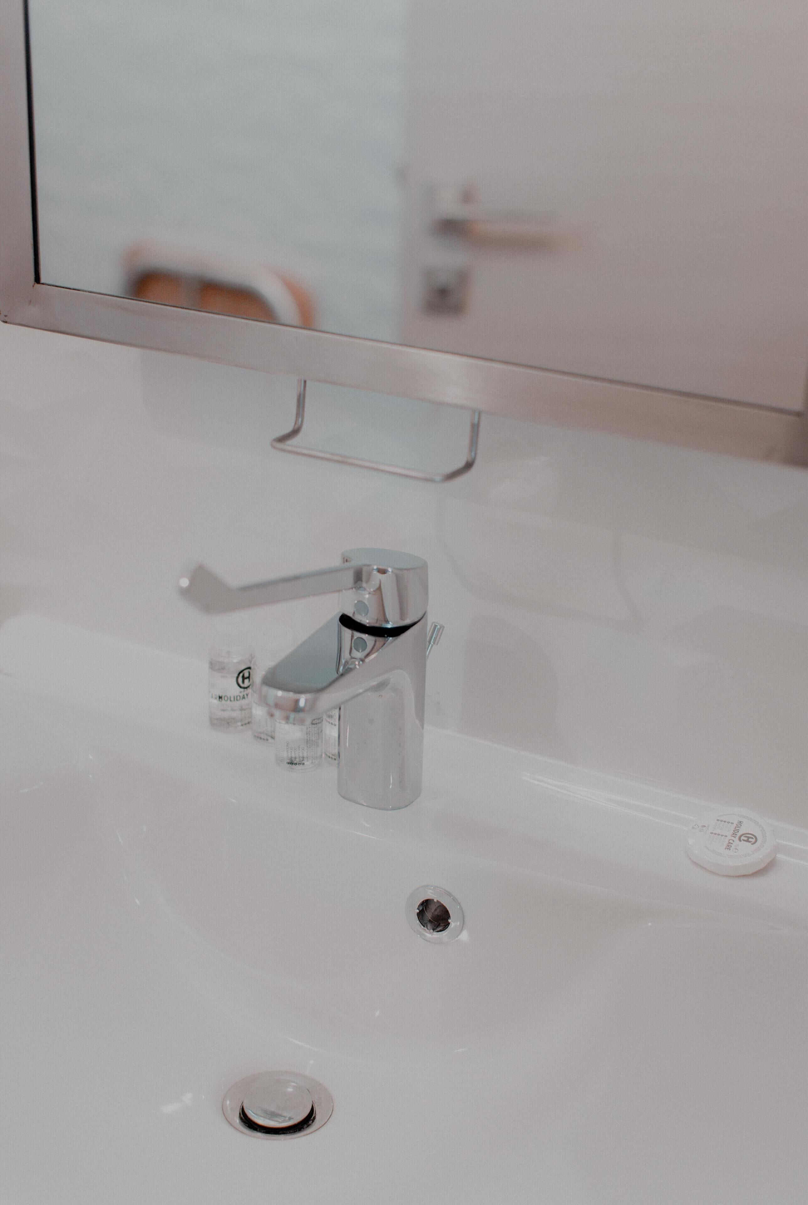 A bathroom sink with a chrome faucet, a mirror above it, and a small bottle of hand soap on the sink's edge.