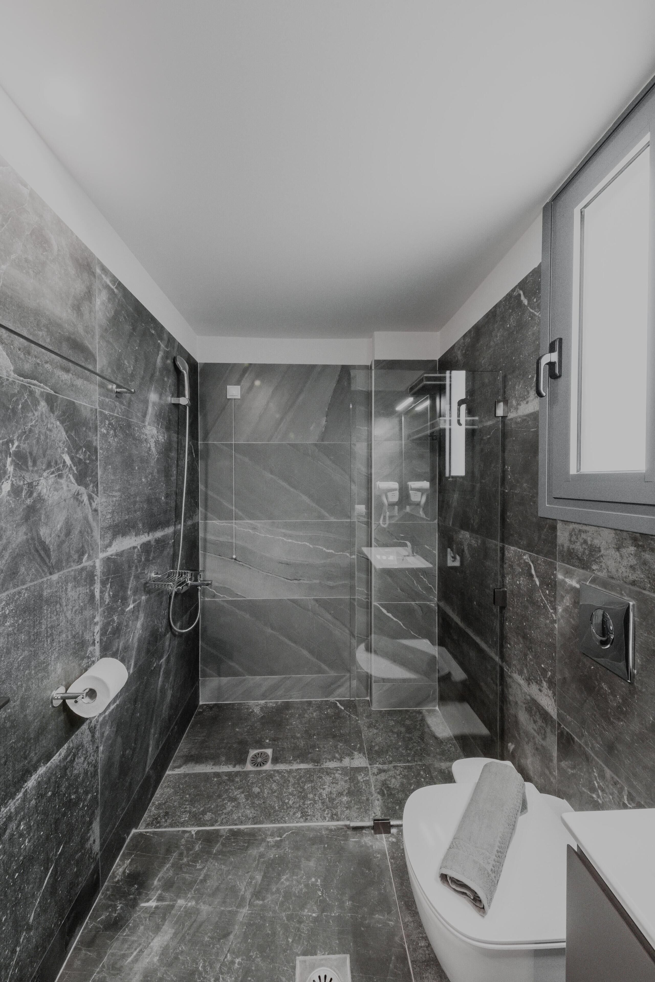 A modern bathroom with a glass-enclosed shower, marble walls, and a white toilet.