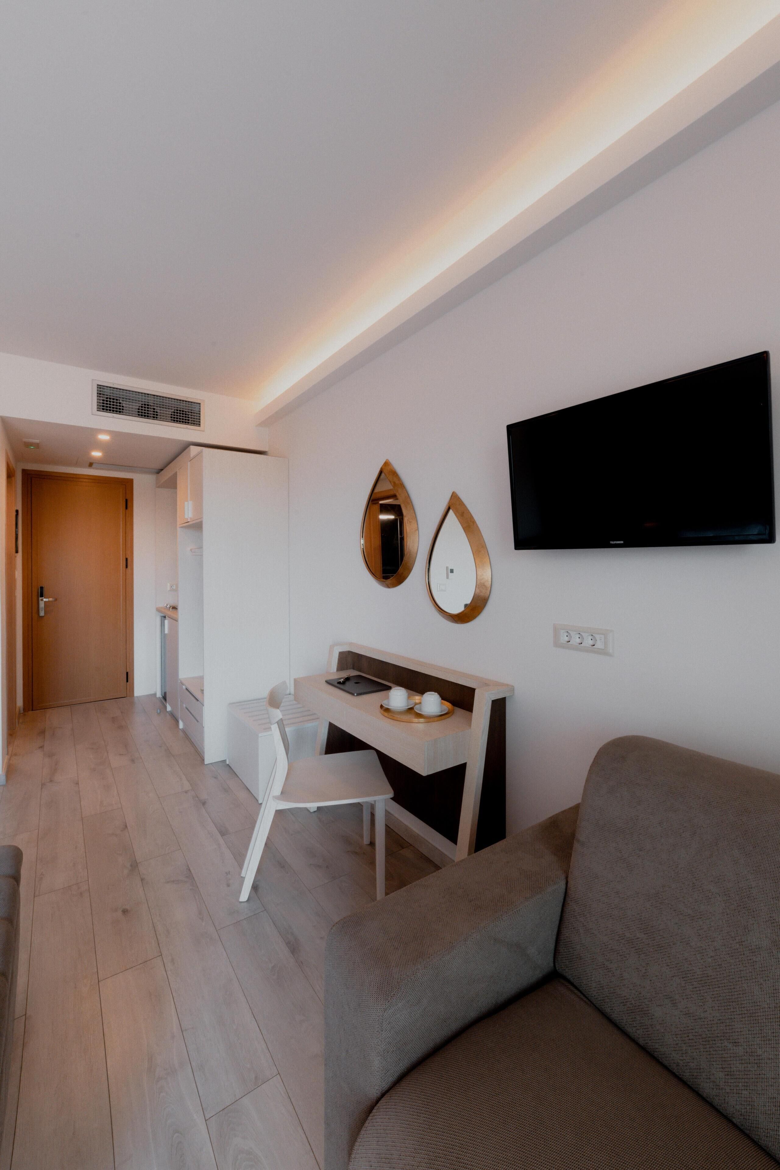 Een moderne woonkamer met een grijze bank, een wit bureau en een wandgemonteerde televisie.