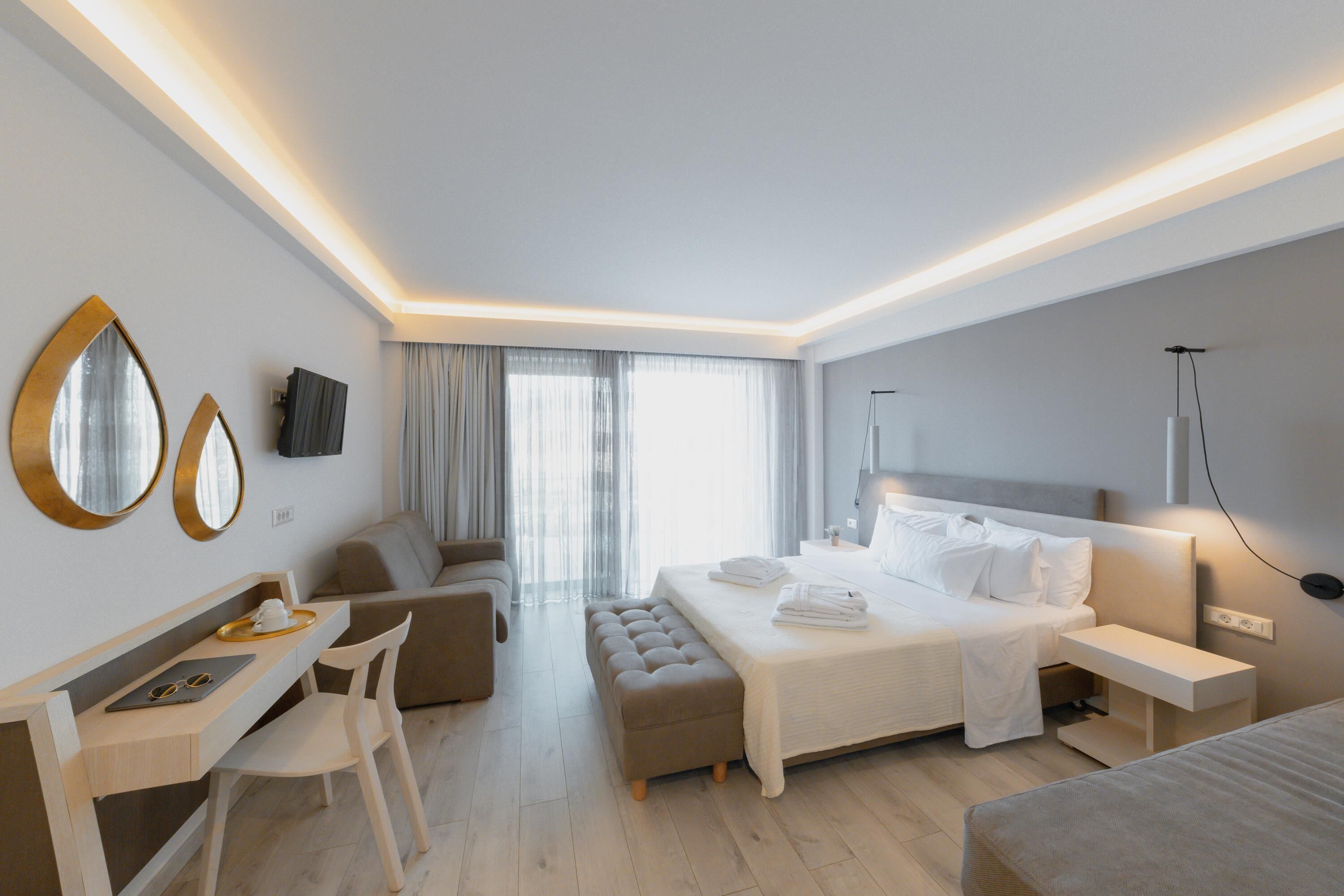 A modern hotel room with a bed, a desk, a chair, a sofa, and a large window with curtains.