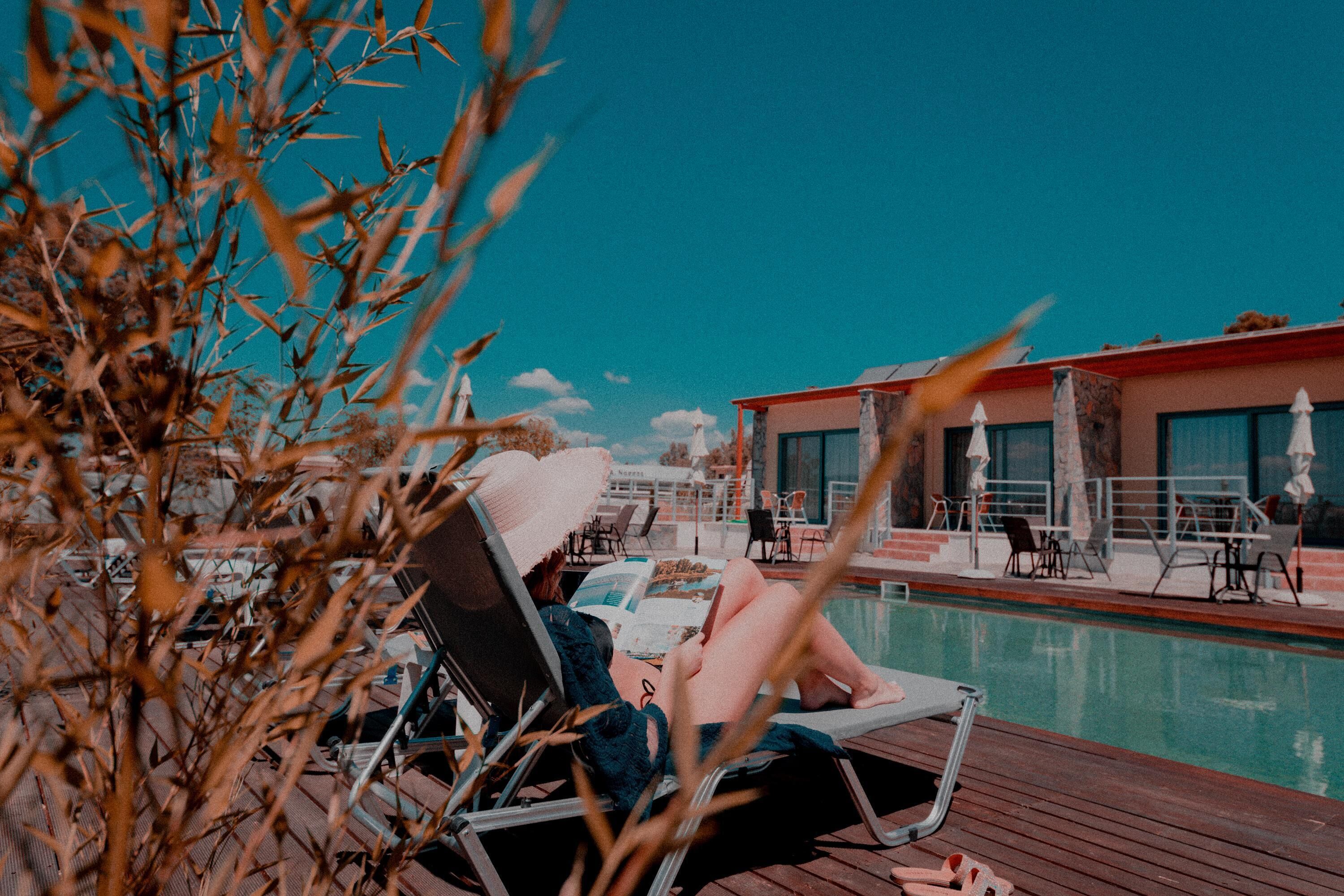 A poolside area with lounge chairs and umbrellas, a pool, and a building with large windows.