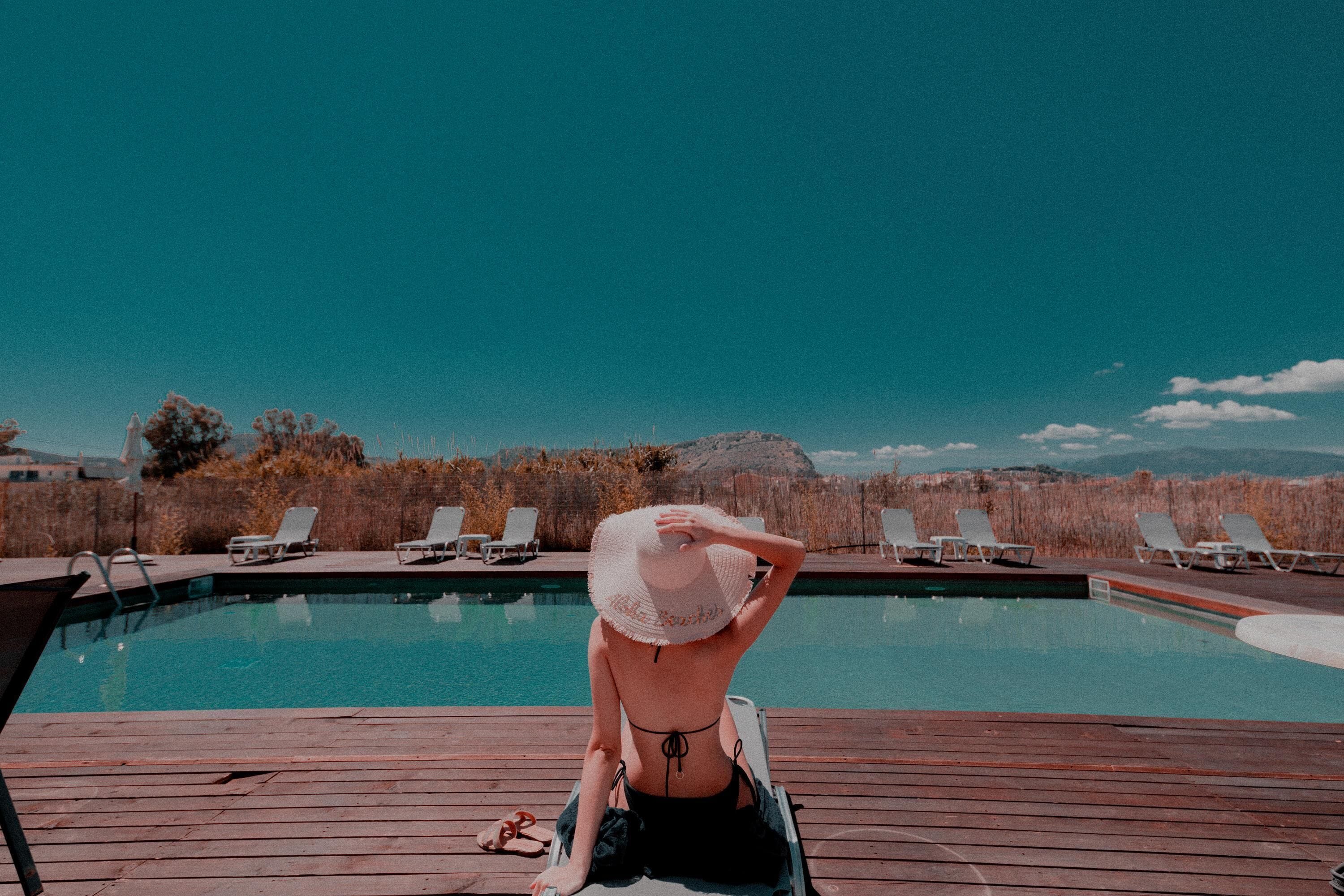 A poolside area with a wooden deck, lounge chairs, and a view of a mountain range.