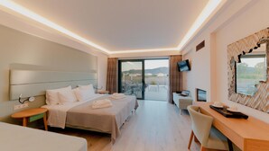 A hotel room with a bed, a desk, a chair, a TV, and a balcony with a view. - Palacio Del Sol Luxury Apartments (Nafplio)
