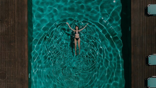 A person floating in a rectangular pool with a wooden deck surrounding it. - Palacio Del Sol Luxury Apartments (Nafplio)