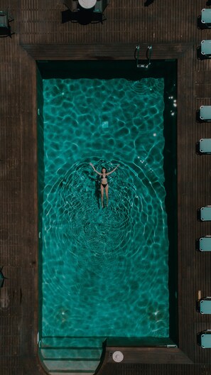 A person floating in a rectangular pool with a wooden deck surrounding it. - Palacio Del Sol Luxury Apartments (Nafplio)