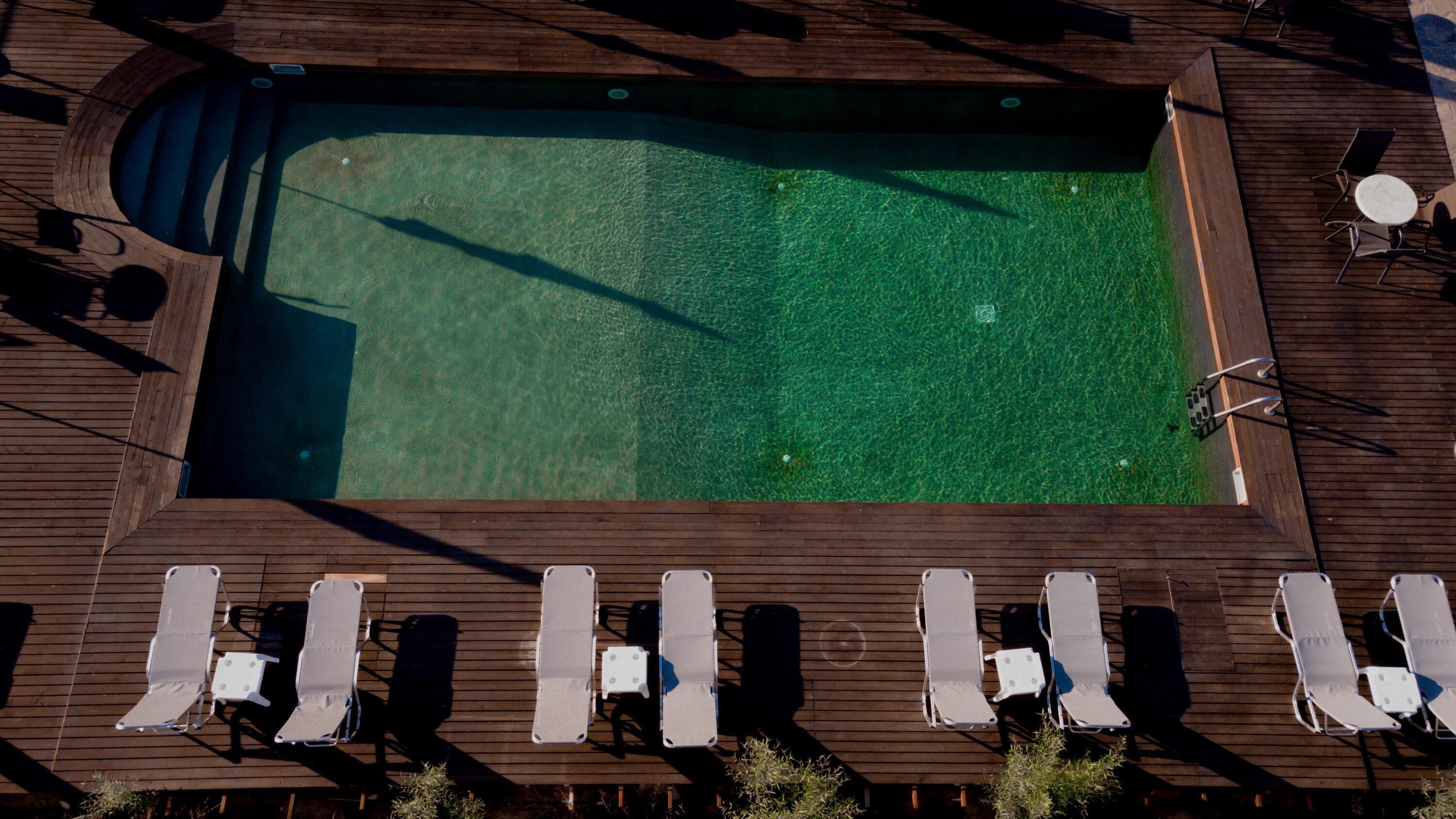 An aerial view of a swimming pool with a wooden deck, surrounded by lounge chairs and a small table.