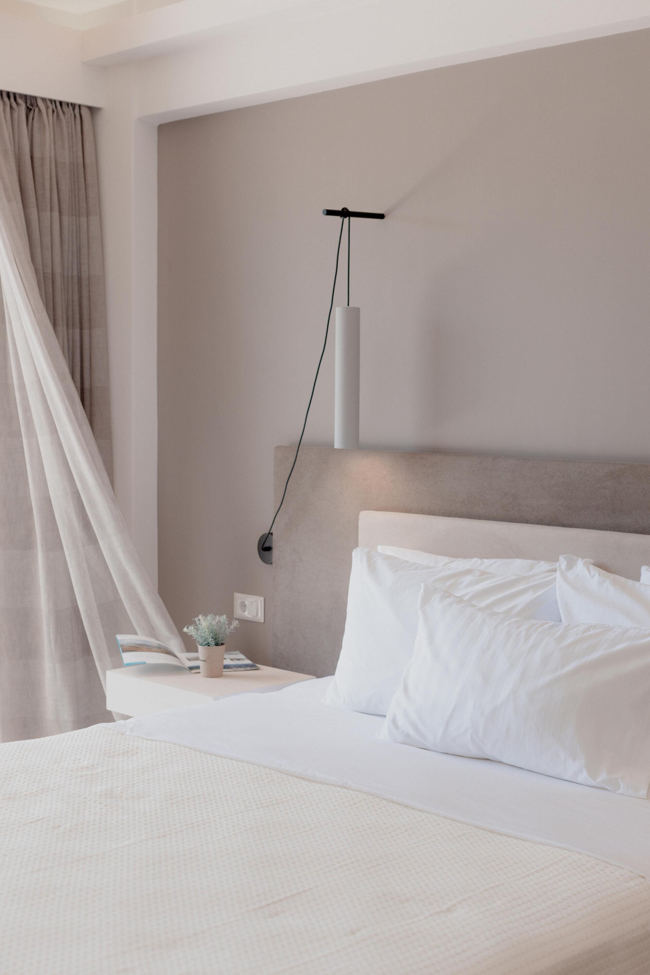 A neatly made bed with white linens, a bedside table with a lamp, and a wall-mounted light fixture.