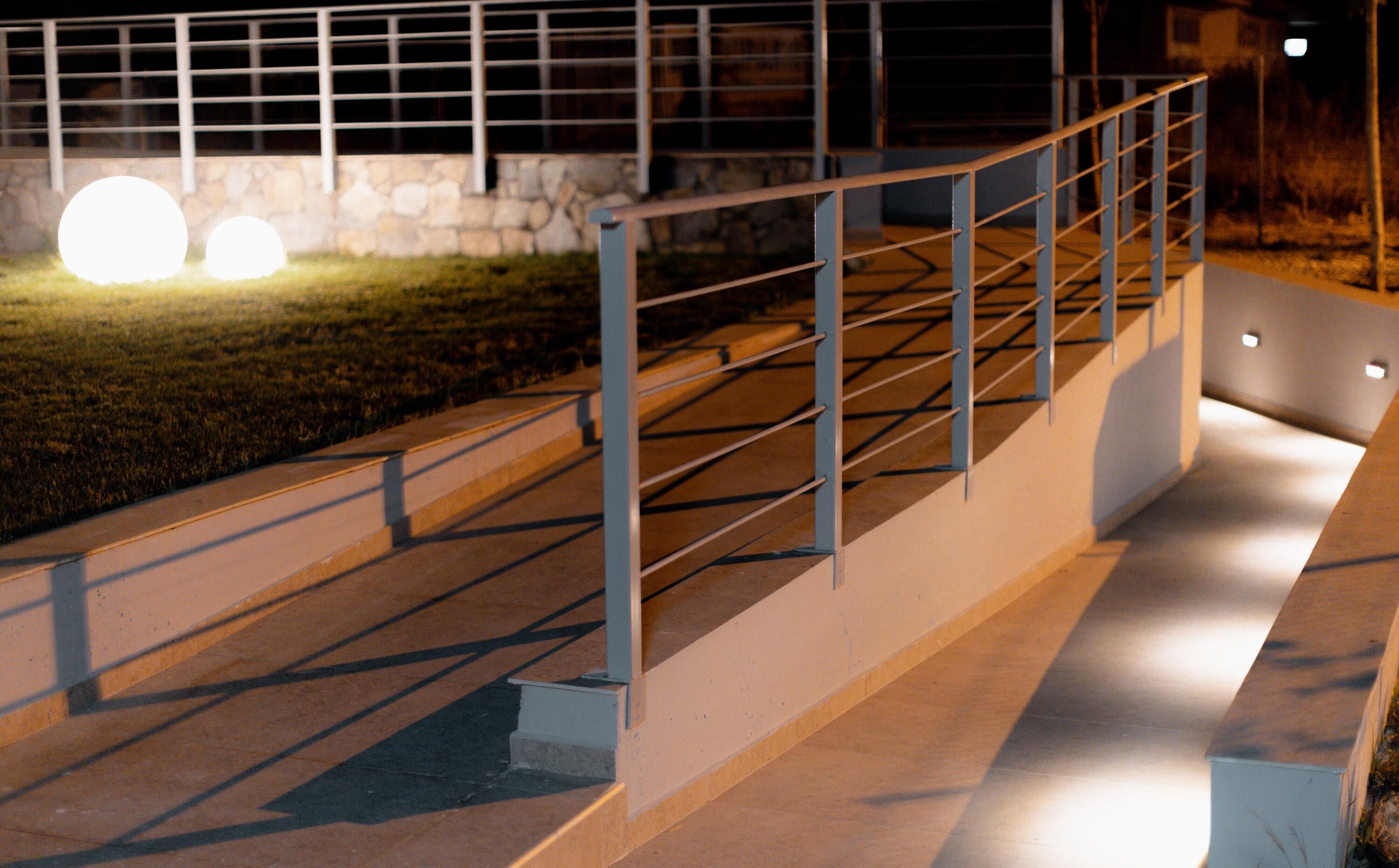 A nighttime outdoor staircase with metal railings, a stone wall, and a grassy area.