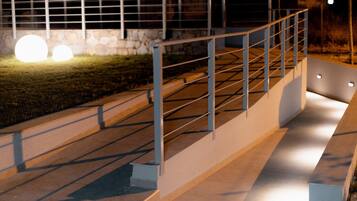 A nighttime outdoor staircase with metal railings, a stone wall, and a grassy area.