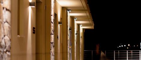A corridor with multiple doors, each illuminated by overhead lights, leading to individual rooms.
