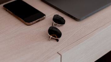 A wooden desk with a smartphone, a pair of sunglasses, and a laptop.
