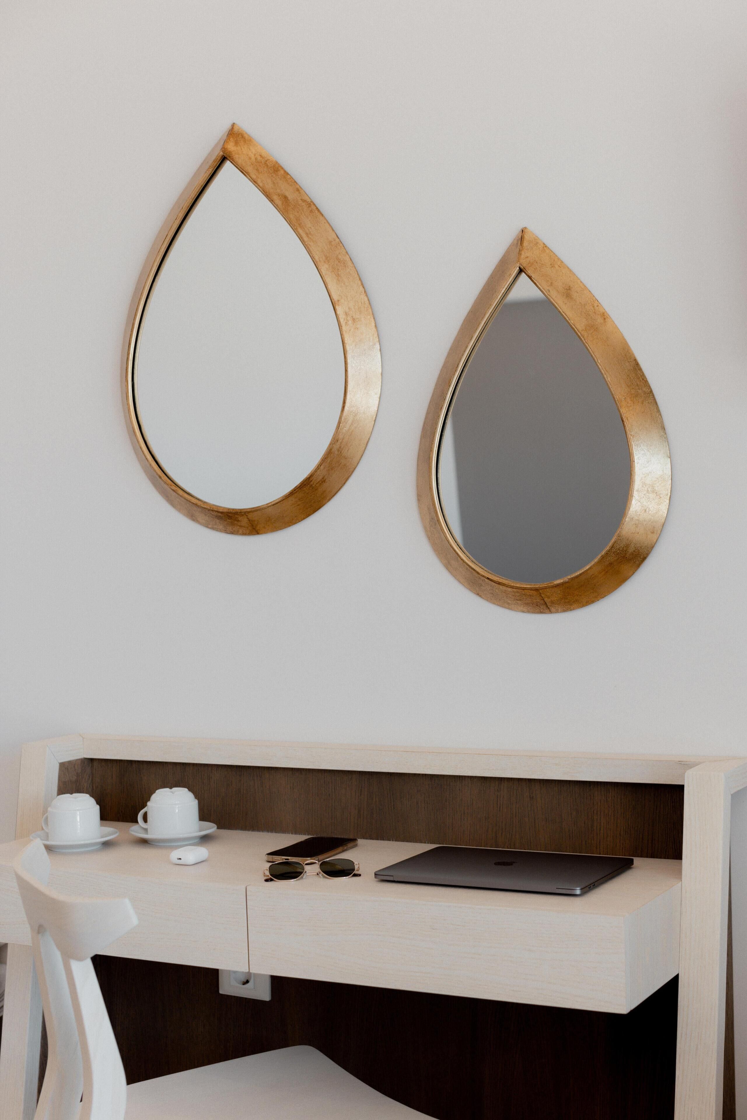 A modern bathroom with a wooden vanity, two gold-framed mirrors, a white chair, a laptop, and a cup and saucer on the counter.
