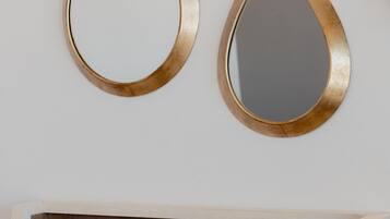 A modern bathroom with a wooden vanity, two gold-framed mirrors, a white chair, a laptop, and a cup and saucer on the counter.