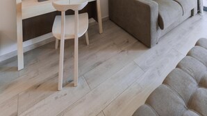 A modern living room with a sofa, a desk with a chair, a television, and a large window with curtains. - Palacio Del Sol Luxury Apartments (Nafplio)