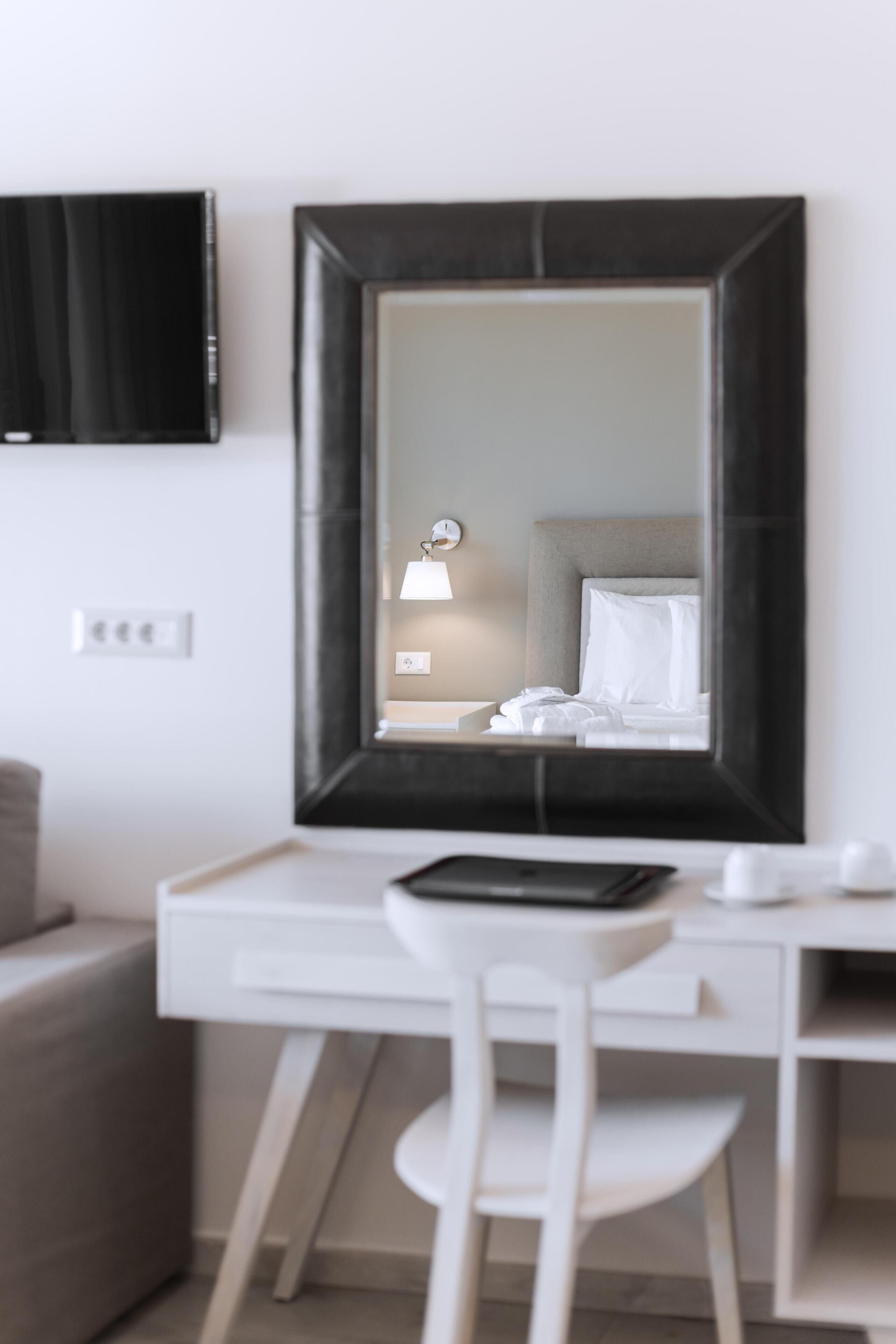 A modern hotel room with a large mirror, a desk, a chair, and a bed with white linens.