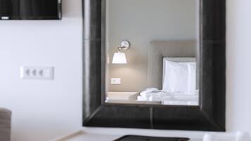 A modern hotel room with a large mirror, a desk, a chair, and a bed with white linens.