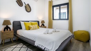 Ein ordentlich eingerichtetes Schlafzimmer mit Bett, Nachttischlampen, einem Fenster mit Vorhängen und einer Wand-Klimaanlage.