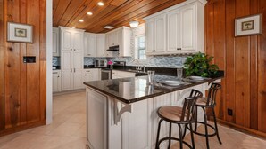 A kitchen with wooden paneling, white cabinets, a marble island with bar stools, and a tiled backsplash.