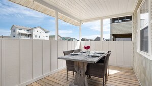 A covered patio with a wooden table set for dining, surrounded by wicker chairs.