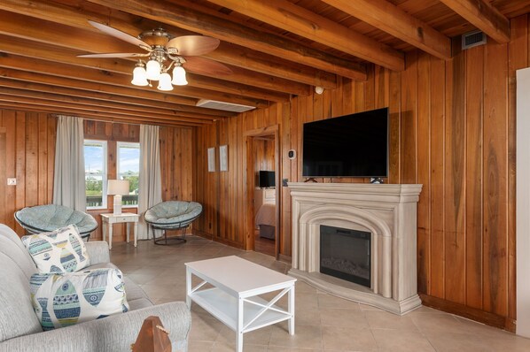 Una sala de estar acogedora con chimenea, paredes de madera, ventilador de techo y televisor montado.