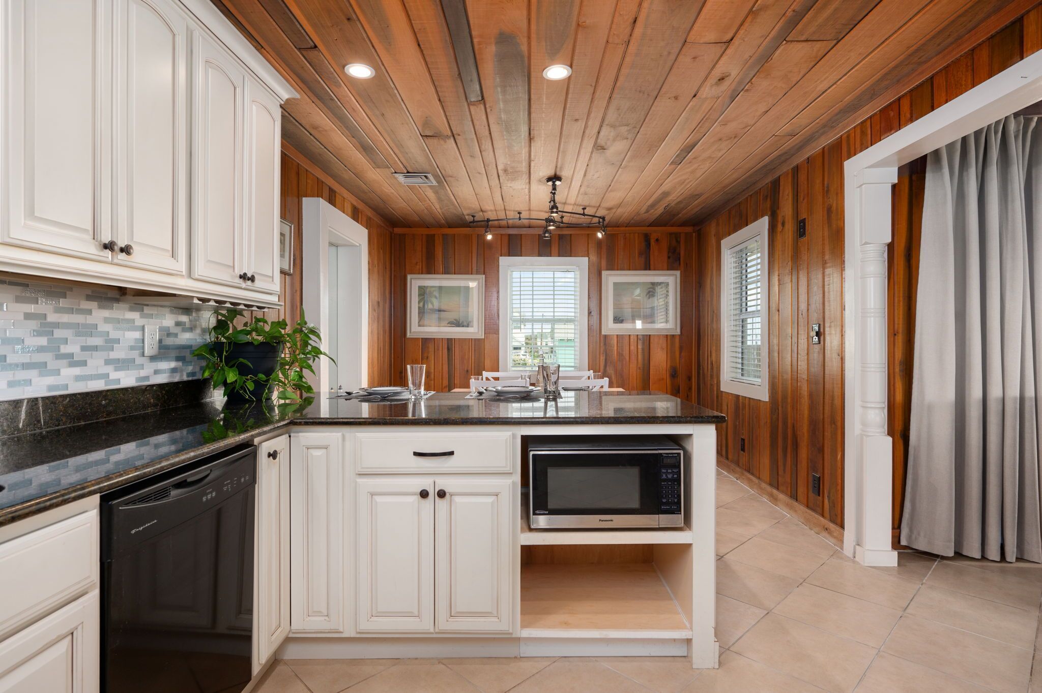 A kitchen with white cabinets, a black countertop, a built-in microwave, and a wooden ceiling.
