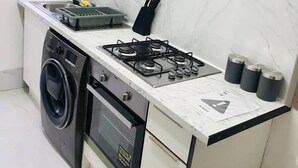 A compact kitchen with a gas stove, a washing machine, and a small sink. - 4 Bedroom Lovely Home in Loughborough Town & Uni (Loughborough)