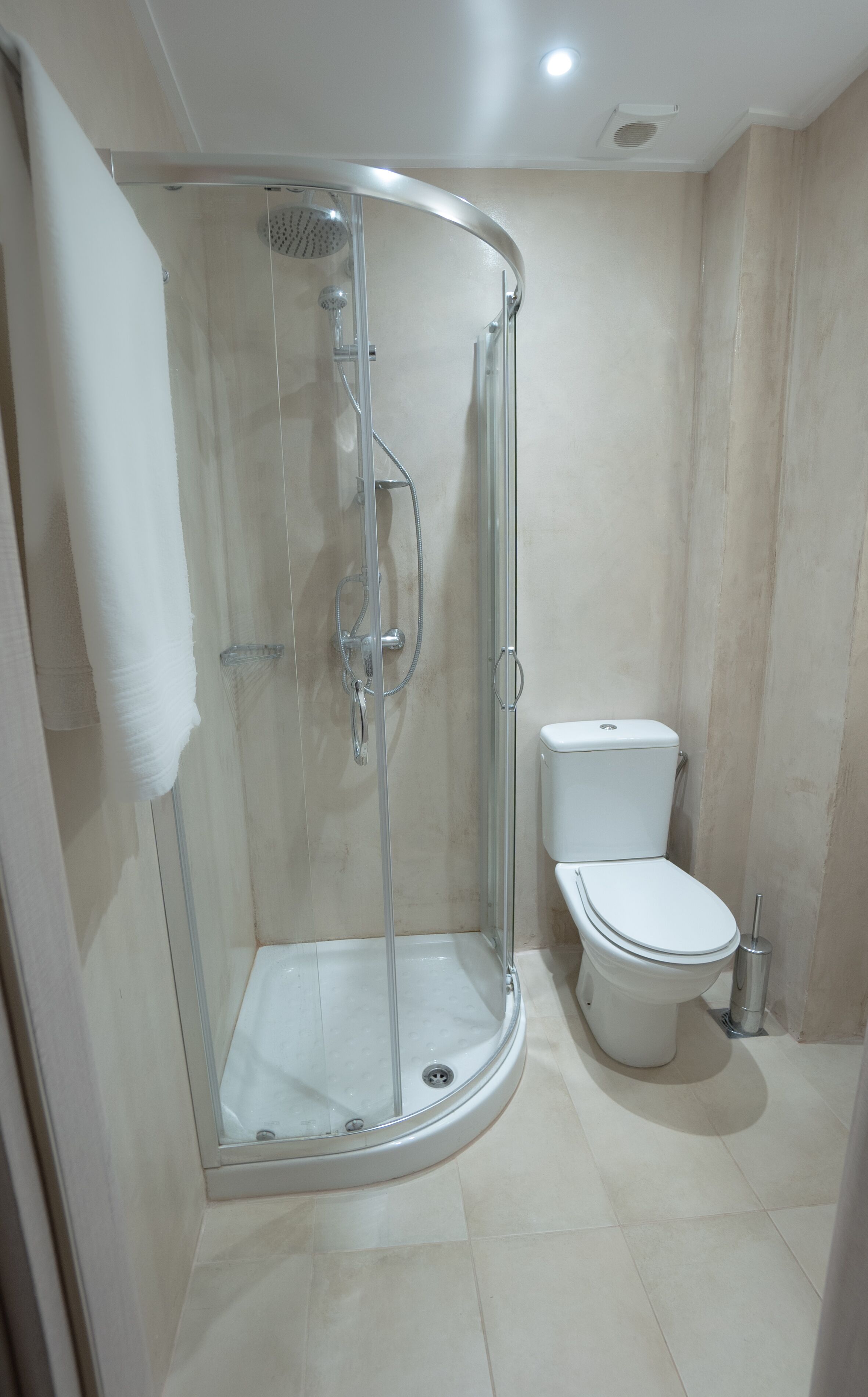 A modern bathroom with a glass-enclosed shower, a toilet, and a towel hanging on the wall.
