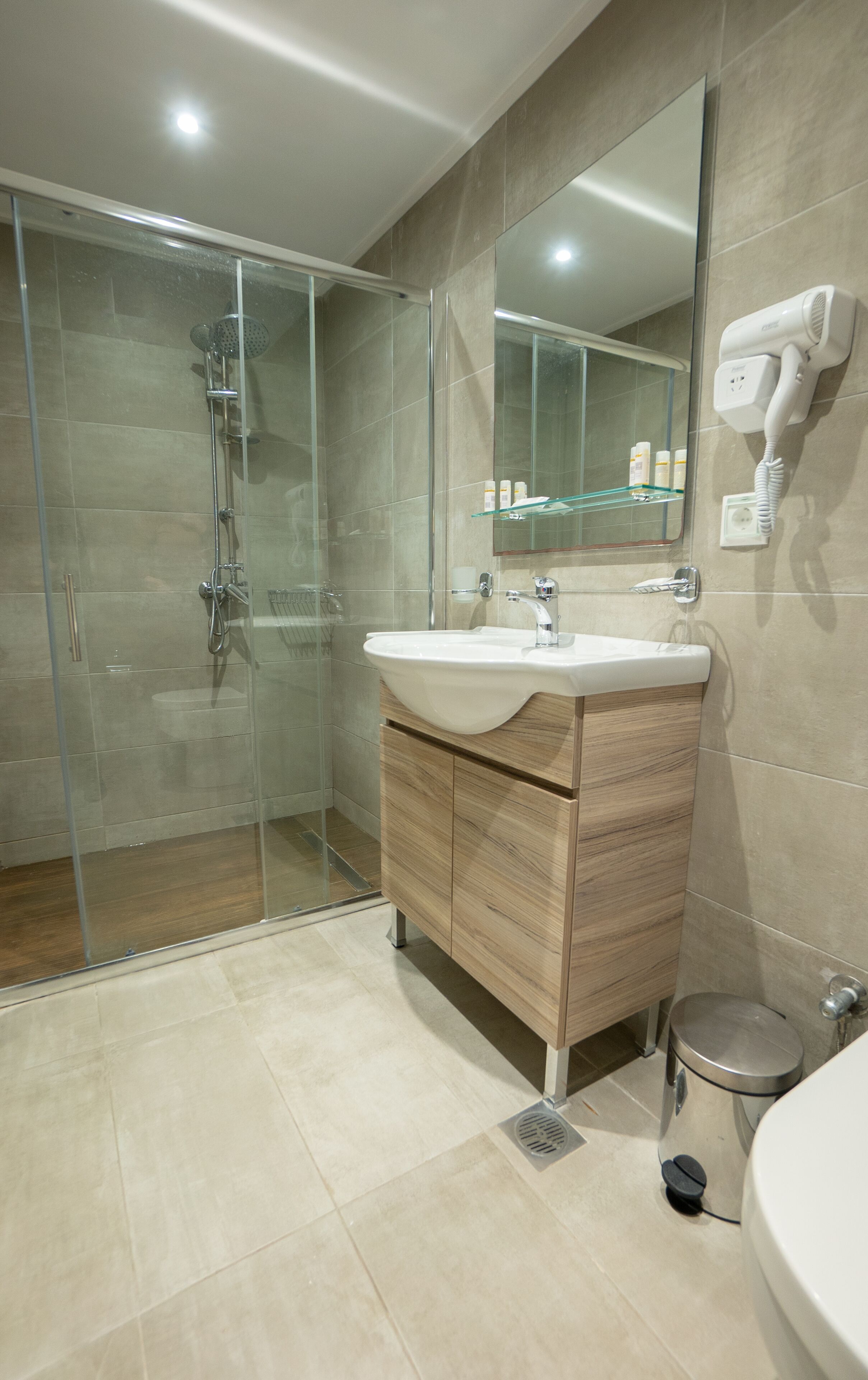 A modern bathroom with a glass shower enclosure, a wooden vanity, and a built-in hairdryer.