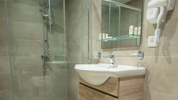 A modern bathroom with a glass shower enclosure, a wooden vanity, and a built-in hairdryer.