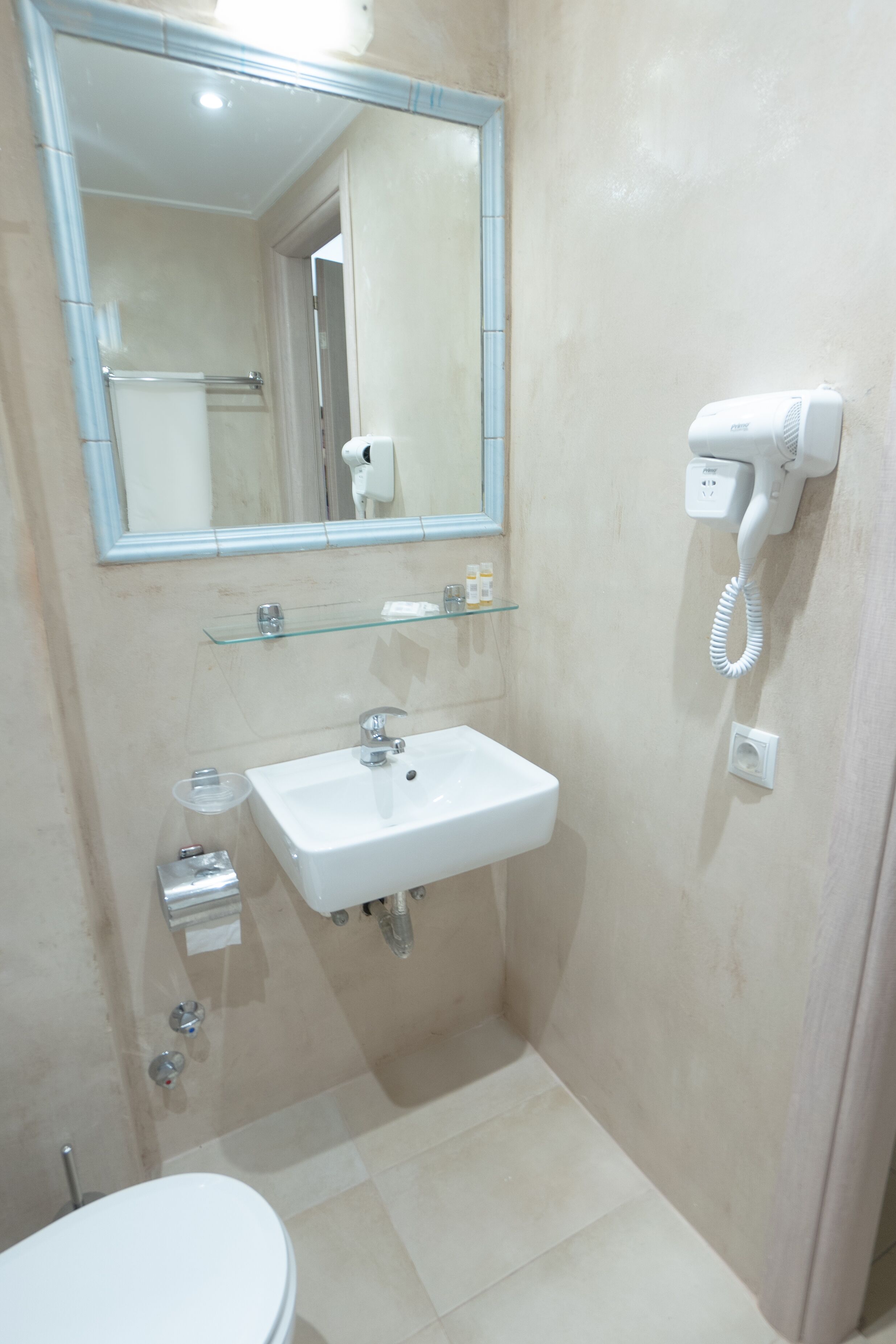 A bathroom with a white sink, mirror, and hairdryer mounted on the wall.
