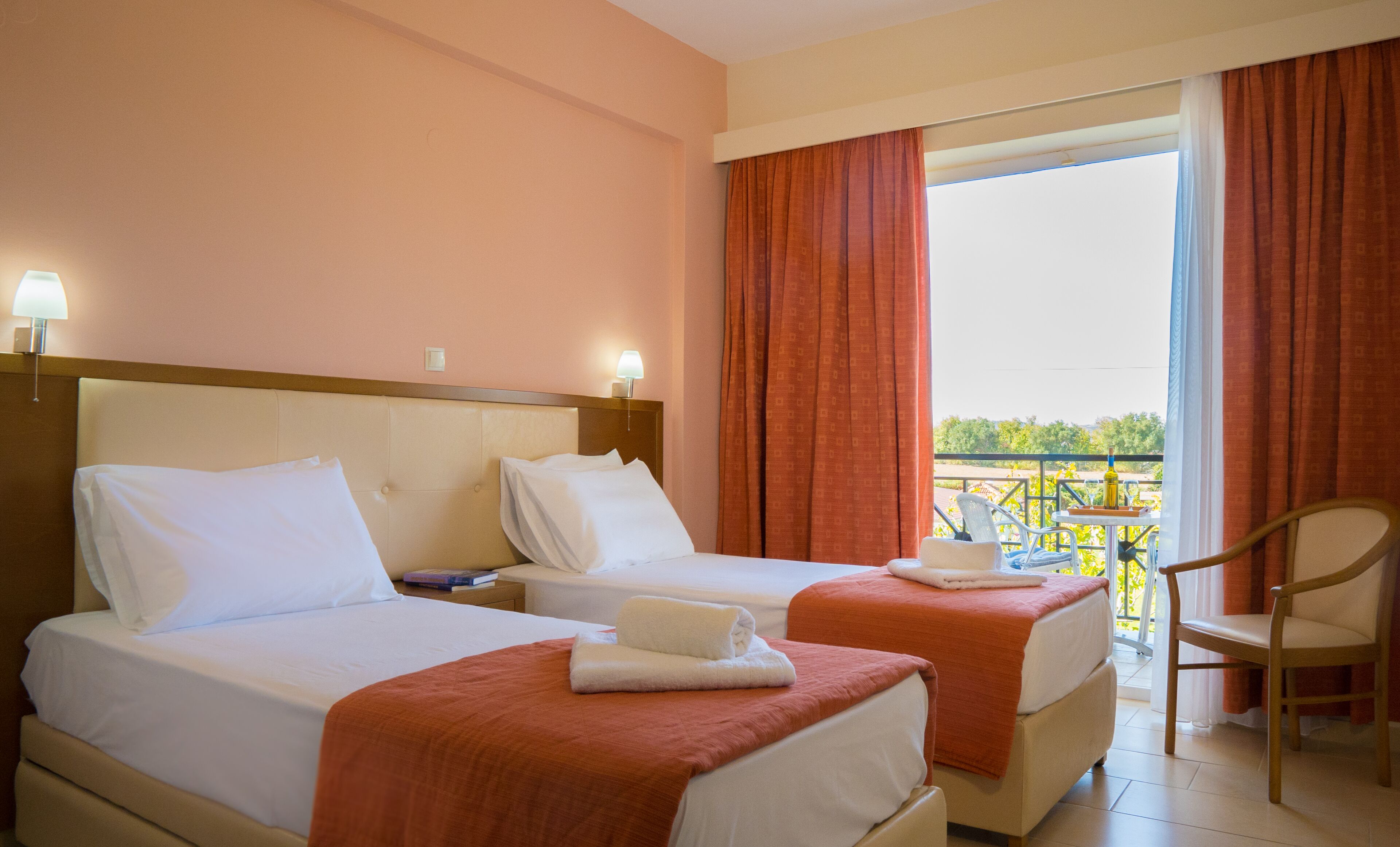 Une chambre d’hôtel avec deux lits, un balcon avec une chaise et une vue sur la verdure.