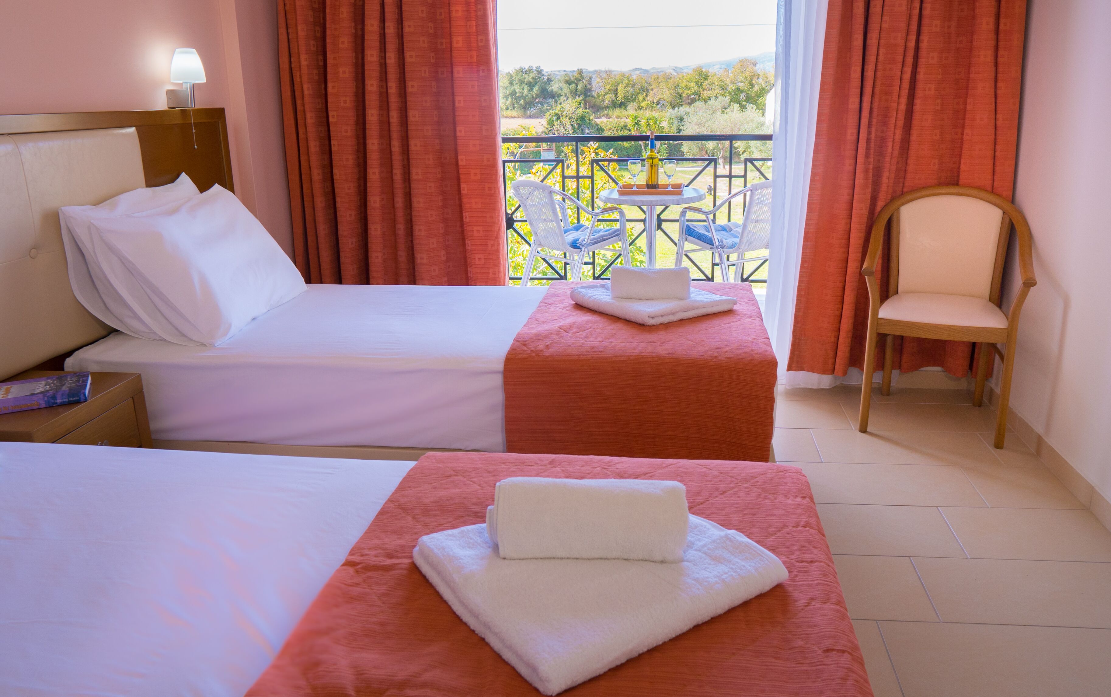 Ein Hotelzimmer mit zwei Betten, einem Sessel und einem Balkon mit Aussicht.