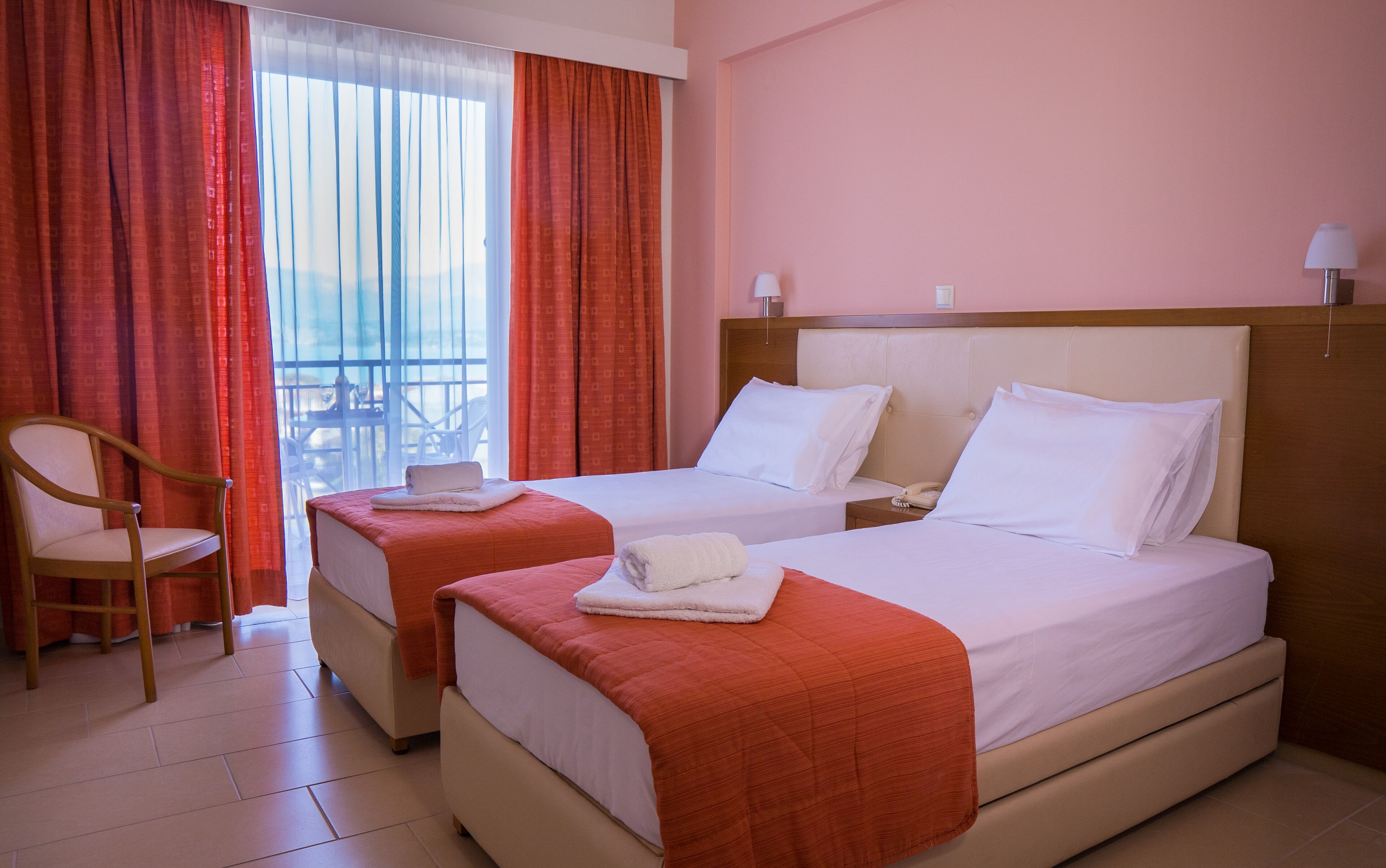A hotel room with two beds, a chair, and a balcony view.