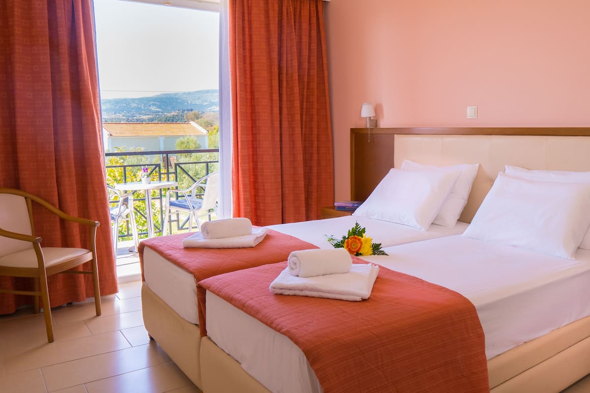 A hotel room with two beds, a balcony with a view, a chair, and a nightstand with a phone.