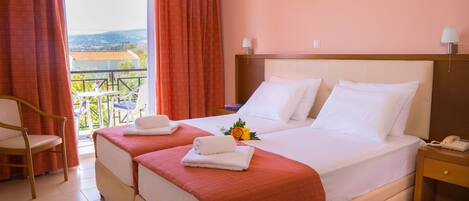 Habitación de hotel con dos camas, un balcón con vistas, una silla y una mesita de noche con un teléfono.