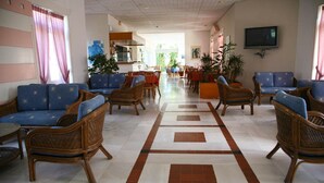 Un hall de hotel con mobiliario de mimbre, suelo de baldosas y un televisor en la pared.
