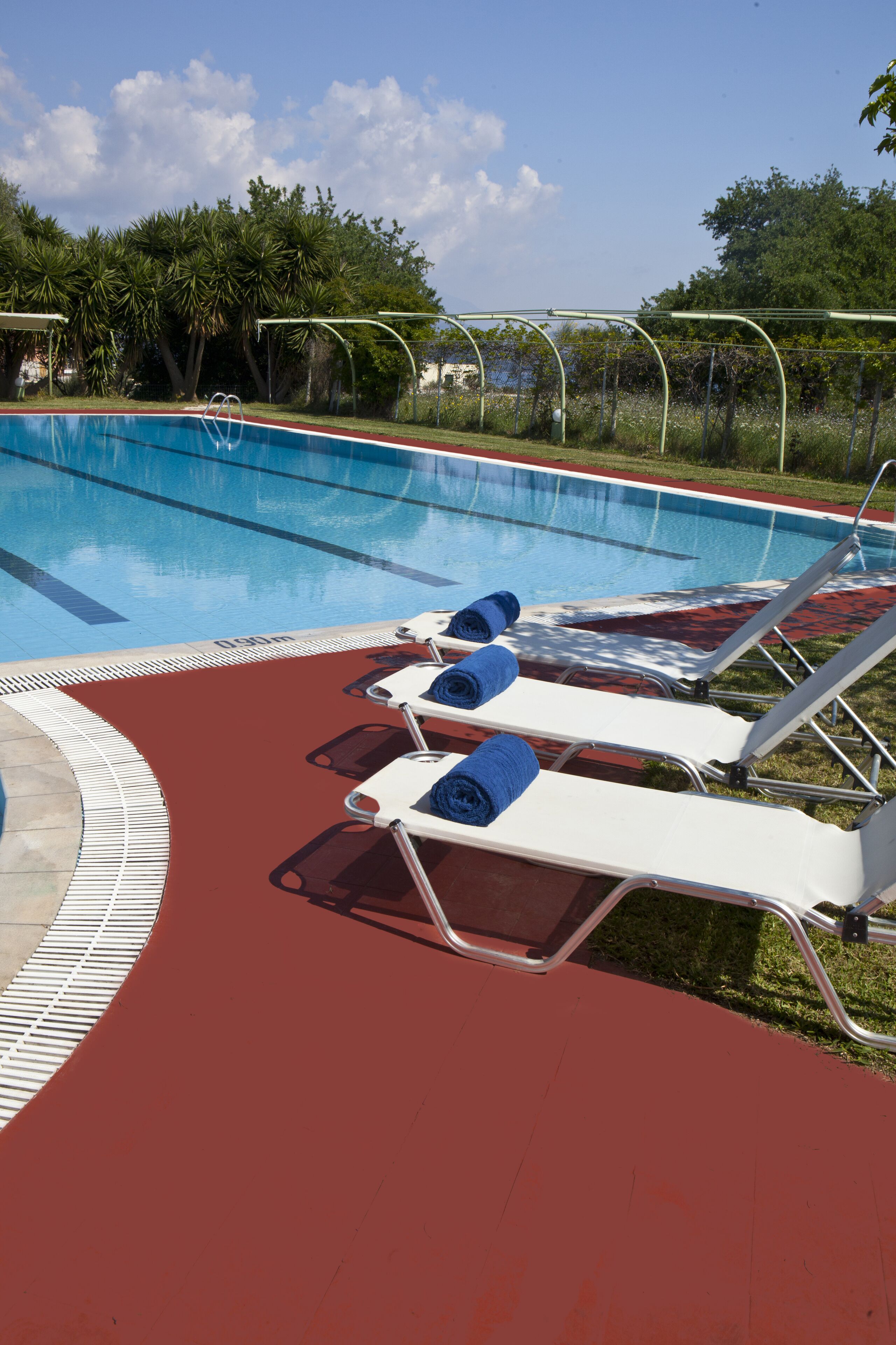 A swimming pool with lounge chairs and towels, surrounded by greenery.