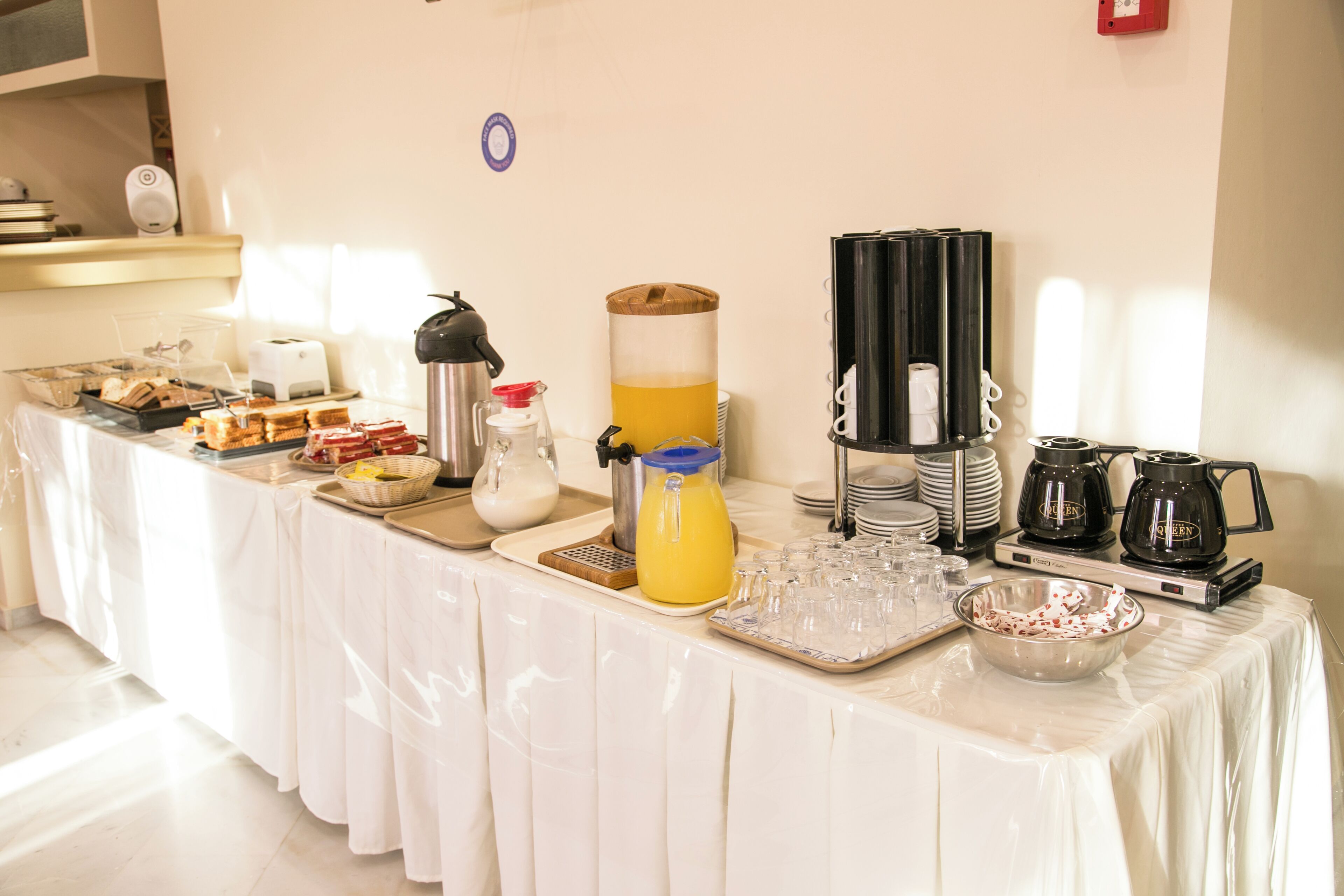 Ein reichhaltiges Frühstücksbuffet mit verschiedenen Speisen, einem Saftspender, Kaffeeautomaten und Gläsern.