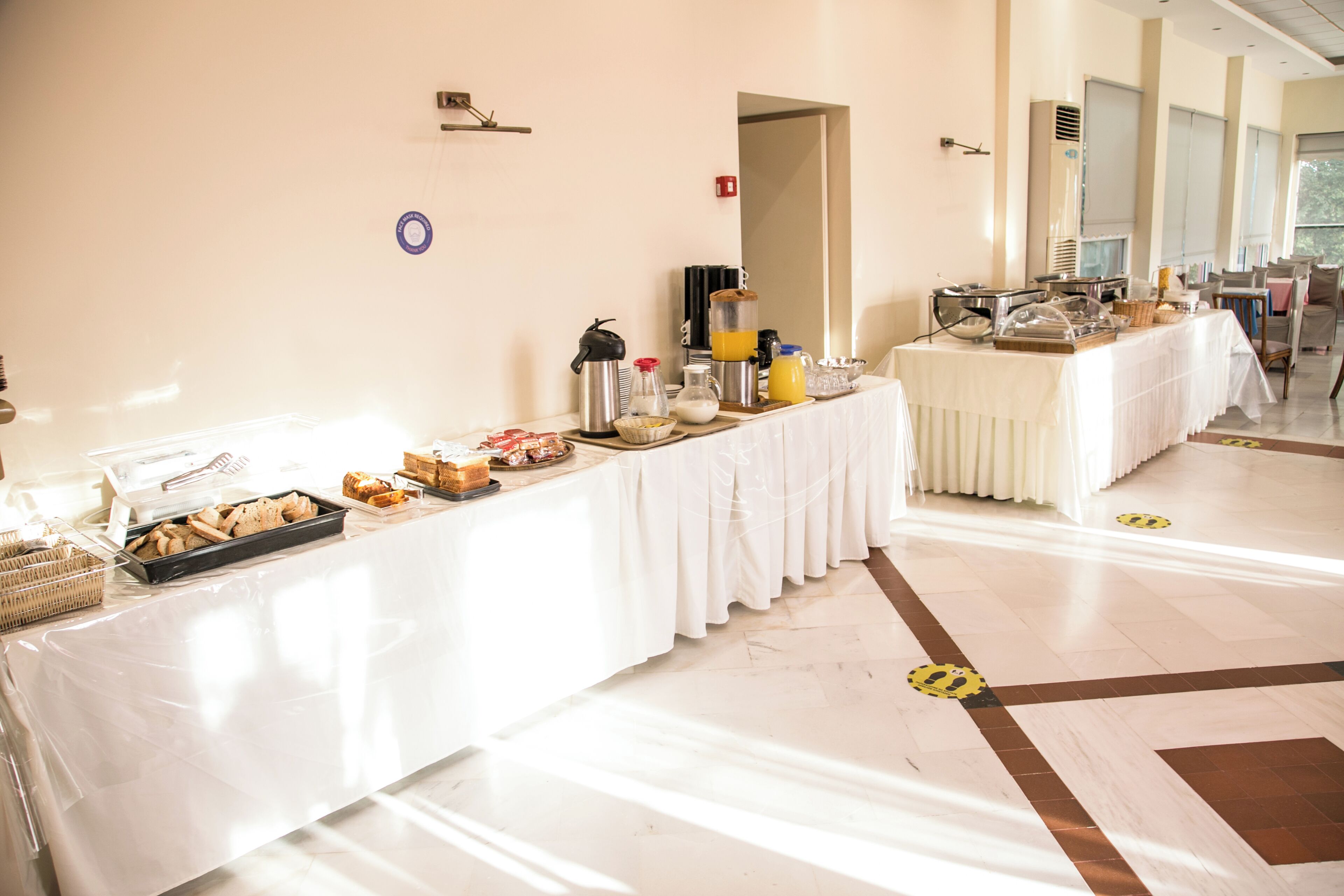 A buffet setup with various food items and beverages, a white tablecloth, and a tiled floor.