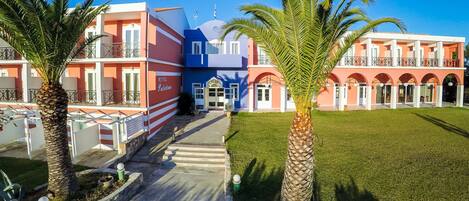 A hotel with a central courtyard, palm trees, and a clear blue sky.