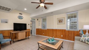 Una sala de estar con televisor, paneles de madera, ventilador de techo y un letrero que dice 'OBX Outer Banks'.