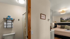 Een hotelkamer met toilet, douche, een bed, een nachtkastje en een wandplank met handdoeken.